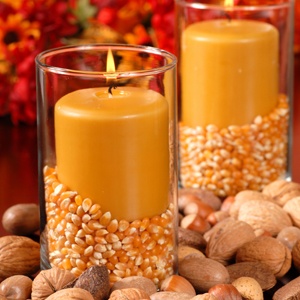 Candle in an autumn setting with corn and nuts